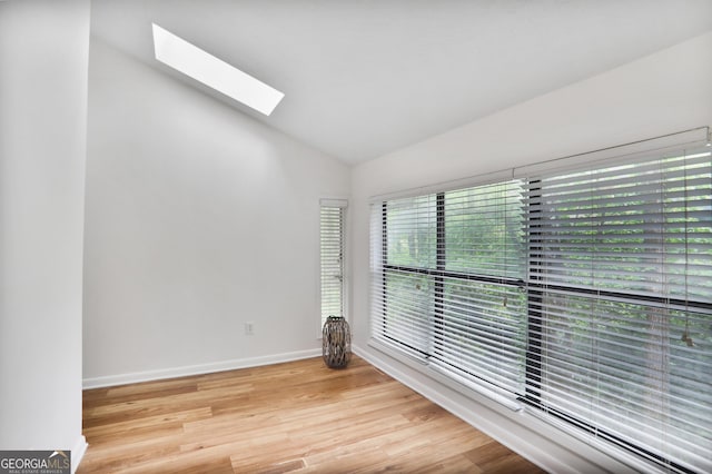 empty room featuring baseboards, light wood finished floors, and vaulted ceiling with skylight