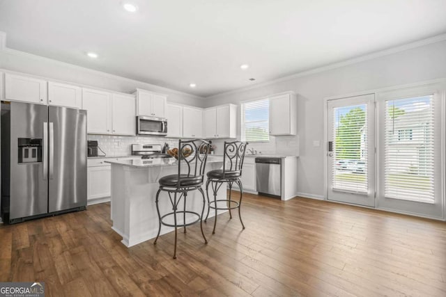 3135 Ellenton Dr, Lithia Springs, GA 30122 - kitchen featuring appliances with stainless steel finishes, a center island, a kitchen bar, ornamental molding, and tasteful backsplash