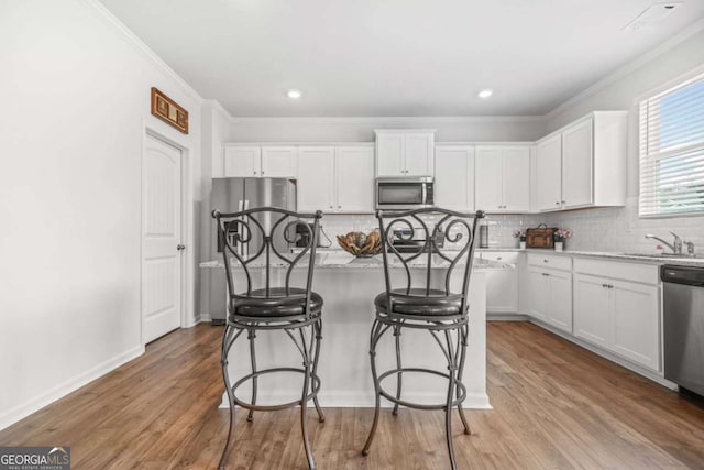 3135 Ellenton Dr, Lithia Springs, GA 30122 - kitchen featuring stainless steel appliances, white cabinetry, a kitchen island, backsplash, and ornamental molding