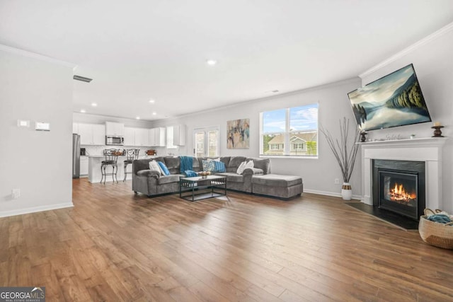 3135 Ellenton Dr, Lithia Springs, GA 30122 - living area featuring crown molding, wood finished floors, a fireplace with flush hearth, and recessed lighting