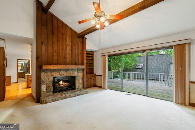 unfurnished living room with beam ceiling, carpet floors, high vaulted ceiling, a stone fireplace, and a ceiling fan