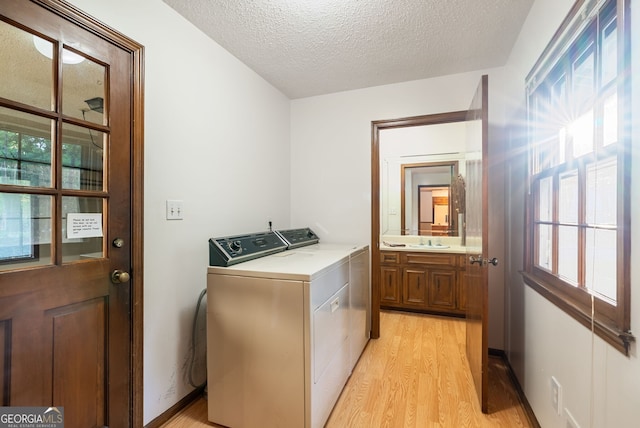 laundry room featuring laundry area, light wood-type flooring, a sink, washer and dryer, and a wealth of natural light