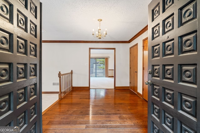 corridor with crown molding, a textured ceiling, a notable chandelier, and hardwood / wood-style floors