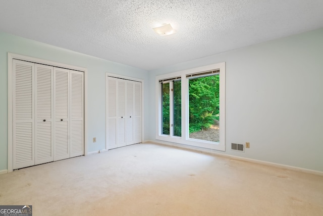 unfurnished bedroom featuring carpet floors, visible vents, two closets, baseboards, and a textured ceiling