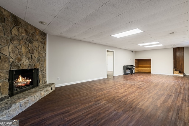 unfurnished living room with a stone fireplace, baseboards, wood finished floors, and a drop ceiling
