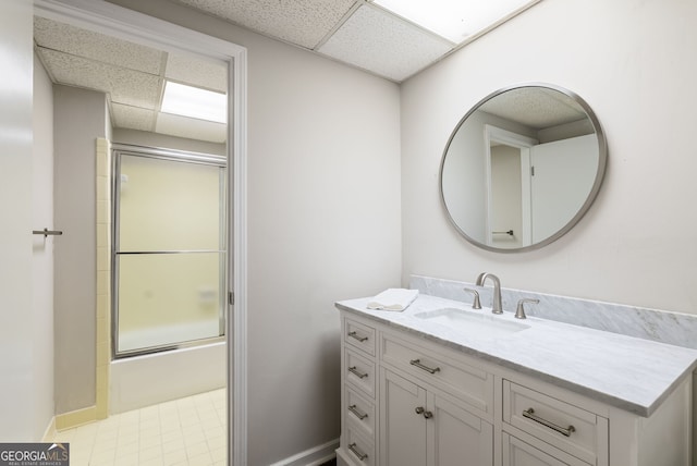 bathroom with vanity, baseboards, combined bath / shower with glass door, and a paneled ceiling