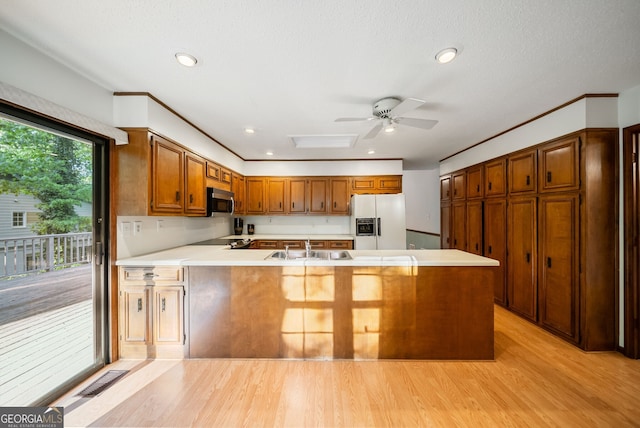 kitchen with a peninsula, white refrigerator with ice dispenser, light countertops, stainless steel microwave, and light wood-style flooring