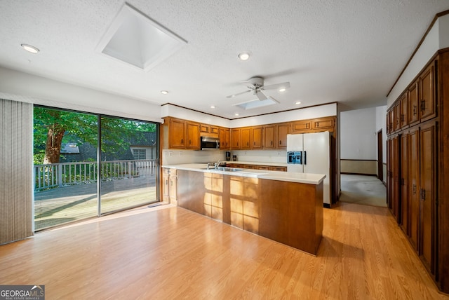 kitchen with light wood-style floors, light countertops, white fridge with ice dispenser, a peninsula, and stainless steel microwave