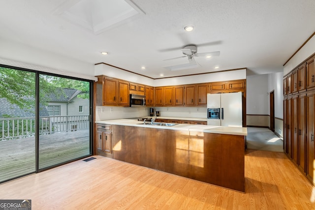 kitchen featuring light countertops, stainless steel microwave, a peninsula, white fridge with ice dispenser, and light wood-style flooring