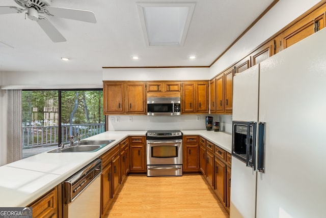 kitchen featuring brown cabinetry, appliances with stainless steel finishes, a sink, light countertops, and light wood finished floors