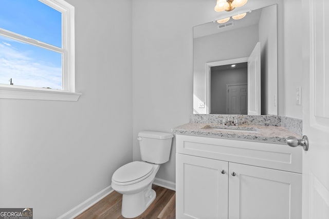 half bathroom featuring visible vents, vanity, wood finished floors, toilet, and baseboards