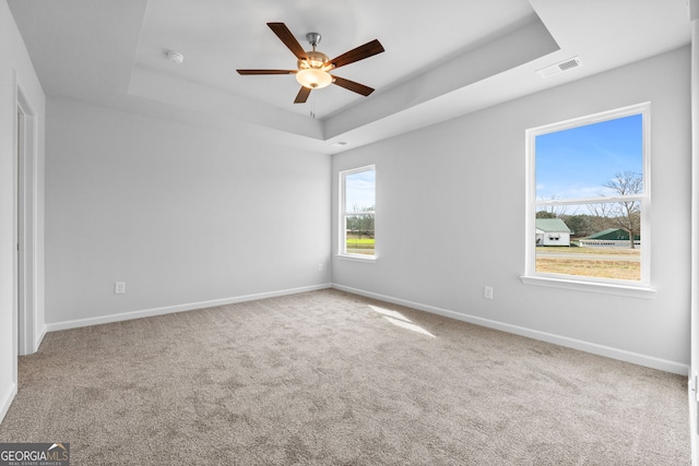 spare room with a raised ceiling, baseboards, a ceiling fan, and visible vents