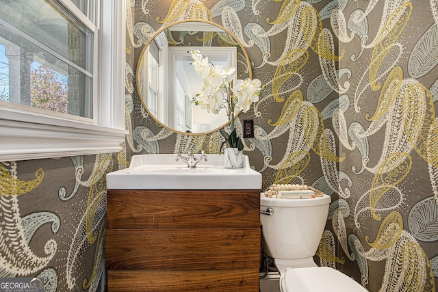 bathroom featuring toilet, wallpapered walls, and vanity