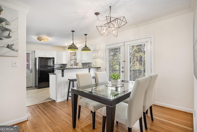 dining area with an inviting chandelier, french doors, light wood-style flooring, baseboards, and ornamental molding