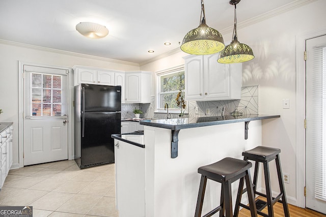 kitchen featuring freestanding refrigerator, a peninsula, dark countertops, a kitchen bar, and white cabinets
