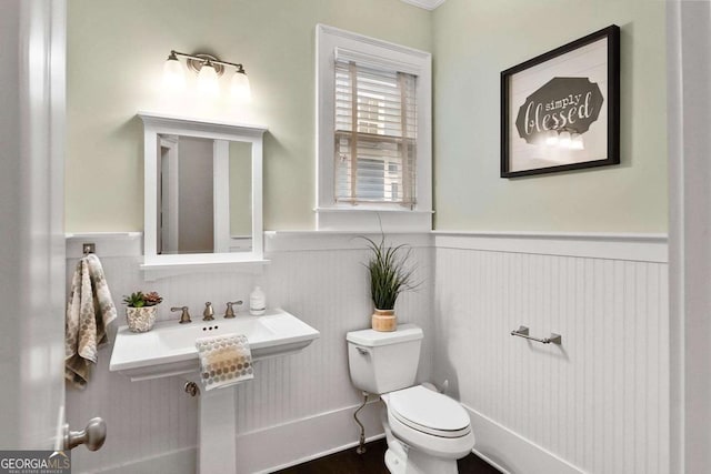 half bathroom with wainscoting, wood finished floors, and toilet