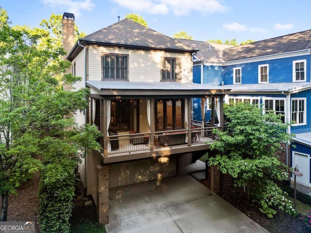 back of property featuring a sunroom, roof with shingles, and a chimney