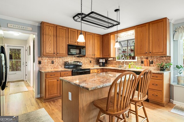 kitchen with crown molding, light stone counters, a sink, light wood-style flooring, and black appliances
