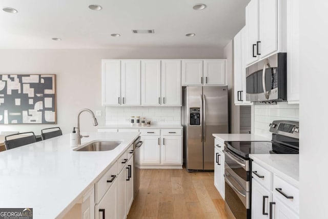 kitchen with visible vents, decorative backsplash, a sink, light wood-style flooring, and stainless steel appliances