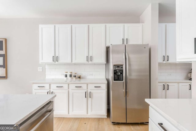 kitchen with light stone countertops, light wood-style floors, stainless steel appliances, white cabinetry, and backsplash