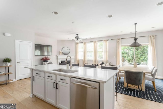 kitchen with stainless steel dishwasher, a healthy amount of sunlight, light wood-style floors, light countertops, and a sink