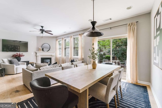 dining space featuring visible vents, a glass covered fireplace, baseboards, ceiling fan, and light wood finished floors