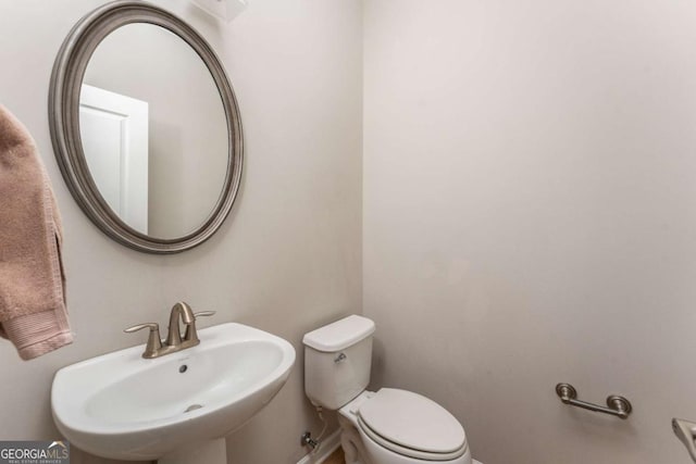 half bathroom with baseboards, a sink, and toilet