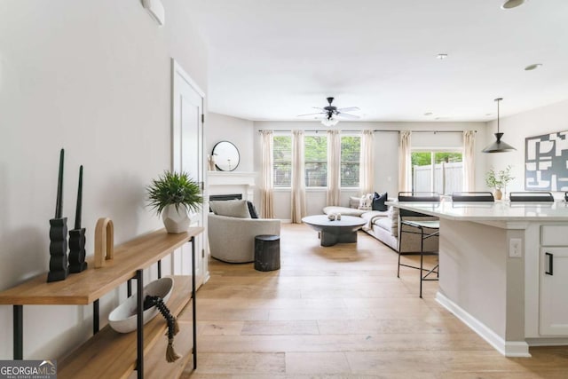 living area with a fireplace, ceiling fan, a wealth of natural light, and light wood-style floors