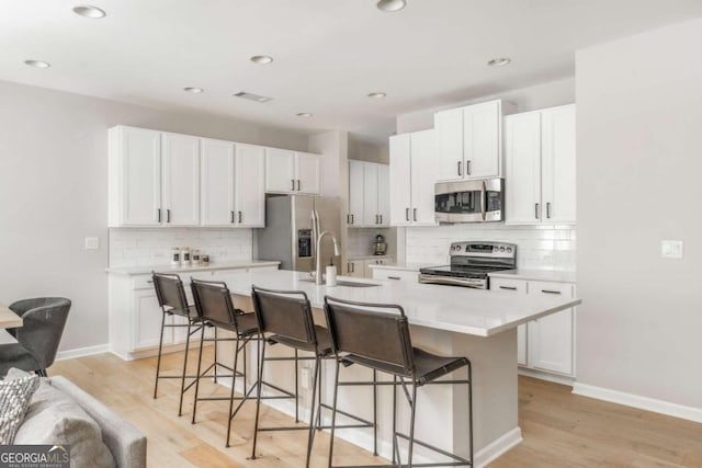 kitchen with a sink, light countertops, a breakfast bar area, stainless steel appliances, and tasteful backsplash