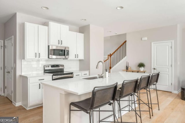 kitchen with light wood-style floors, a kitchen breakfast bar, white cabinetry, a sink, and stainless steel appliances