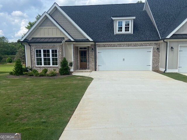 craftsman-style home with board and batten siding, driveway, a front lawn, and brick siding