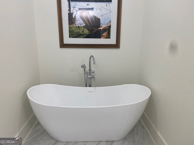bathroom featuring baseboards, a freestanding bath, a sink, and marble finish floor