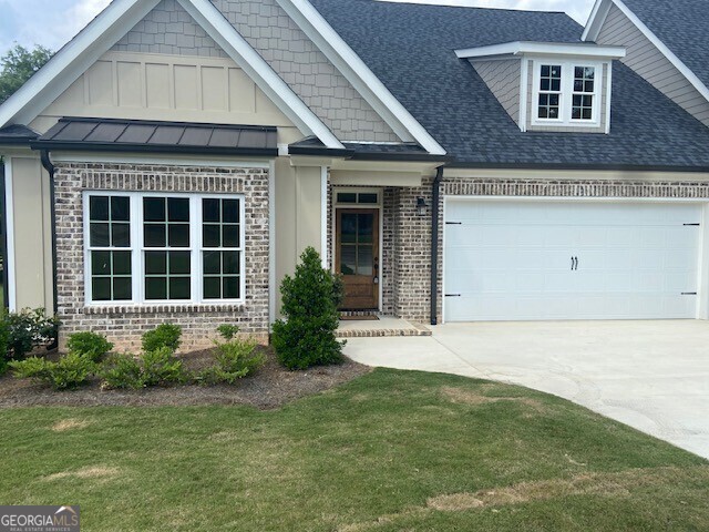 craftsman inspired home featuring a shingled roof, a front lawn, brick siding, a garage, and concrete driveway