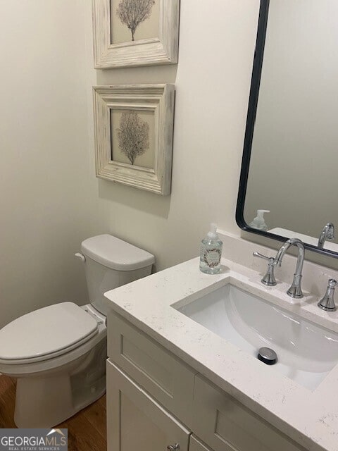 half bathroom featuring toilet, wood finished floors, and vanity