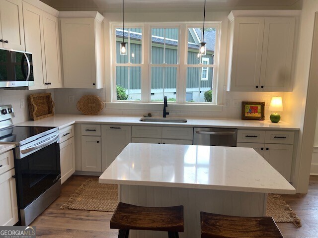 kitchen featuring appliances with stainless steel finishes, a sink, light countertops, a breakfast bar area, and wood finished floors