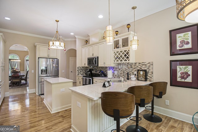 kitchen featuring appliances with stainless steel finishes, a sink, arched walkways, a peninsula, and a kitchen island