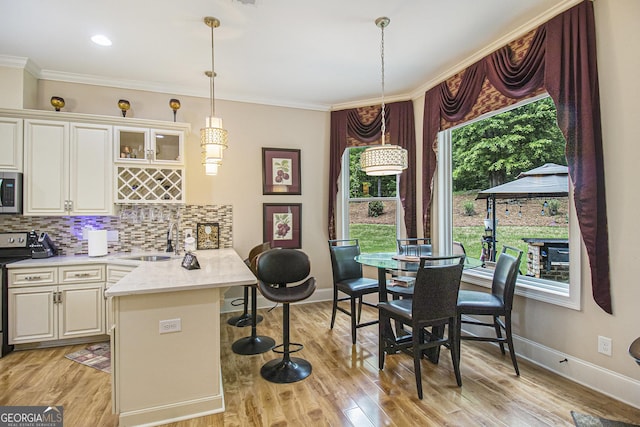 kitchen with crown molding, a peninsula, a breakfast bar area, stainless steel microwave, and a sink