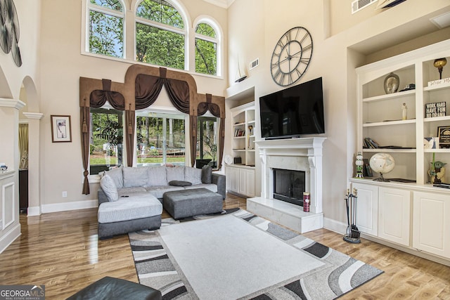 living area with a high ceiling, a fireplace, light wood-style floors, built in features, and visible vents
