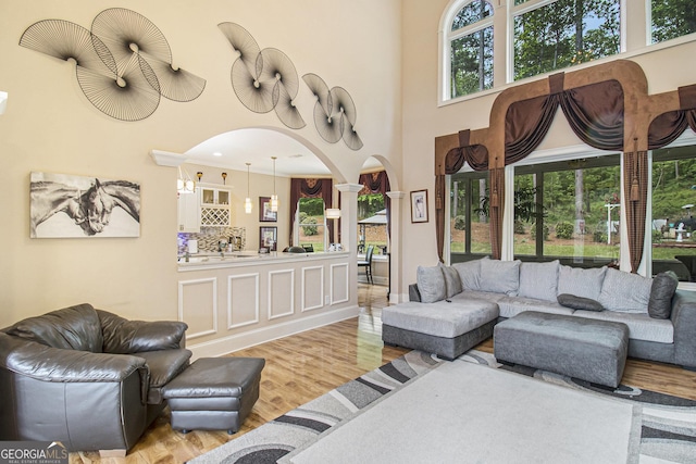 living room with arched walkways, decorative columns, wood finished floors, and a towering ceiling