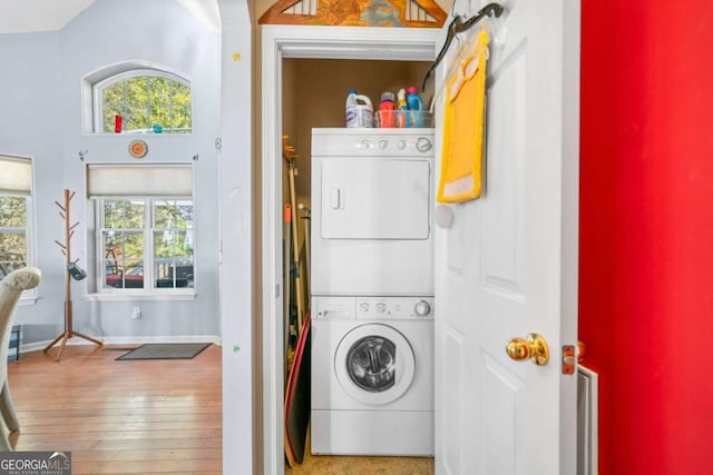 washroom featuring baseboards, wood-type flooring, and stacked washer / dryer