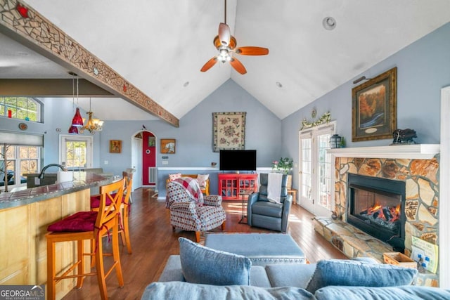 living area with wood finished floors, a fireplace, high vaulted ceiling, arched walkways, and a ceiling fan