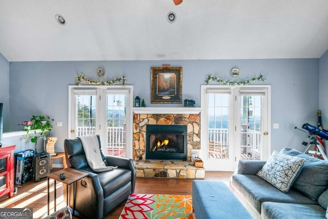 living area with a stone fireplace, wood finished floors, a wealth of natural light, and vaulted ceiling