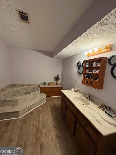 full bathroom with wood finished floors, a textured ceiling, vanity, and a bath