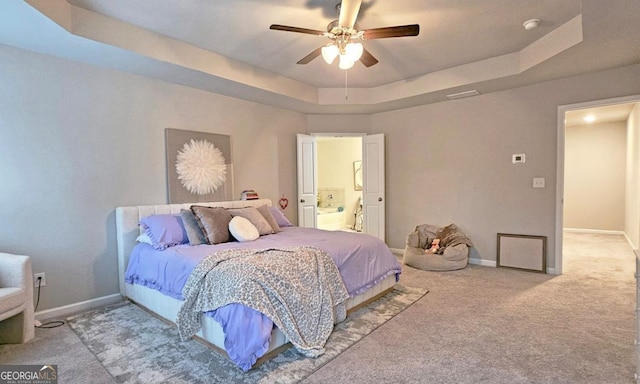 carpeted bedroom with a ceiling fan, a tray ceiling, baseboards, and ensuite bath