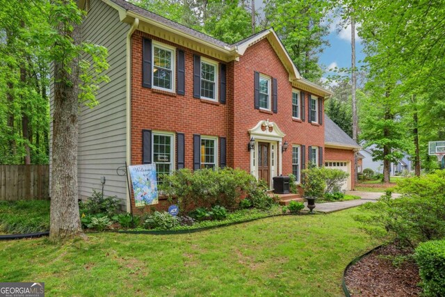 colonial home with a garage, brick siding, fence, cooling unit, and a front lawn