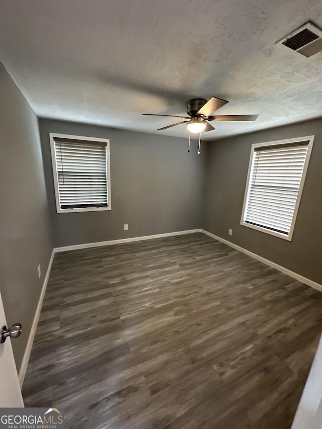 empty room featuring dark wood-style flooring, a ceiling fan, baseboards, and visible vents