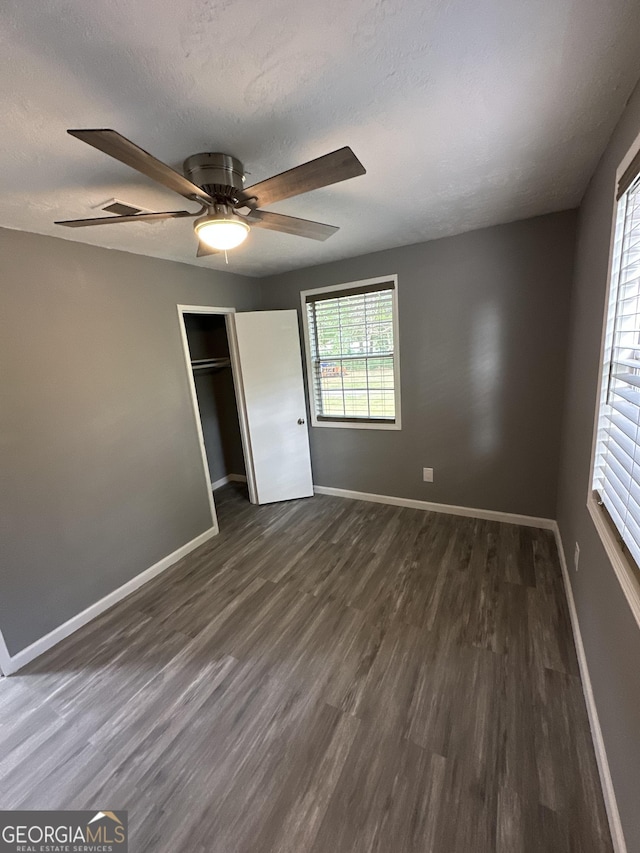 unfurnished bedroom with ceiling fan, a textured ceiling, baseboards, a closet, and dark wood-style floors