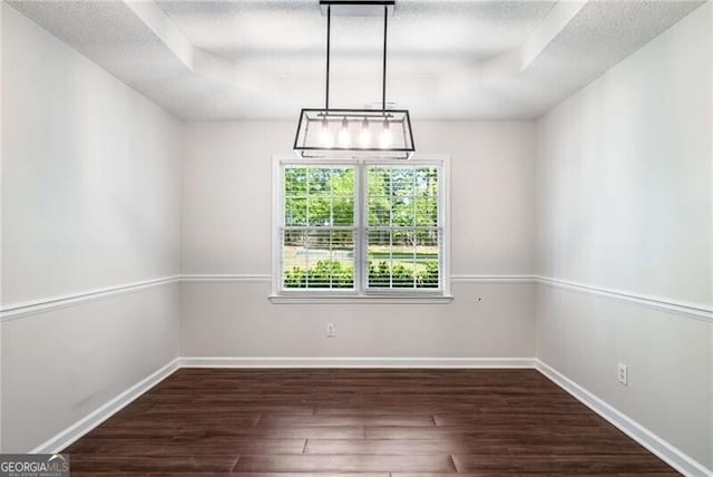 unfurnished dining area featuring baseboards, a textured ceiling, a raised ceiling, and wood finished floors