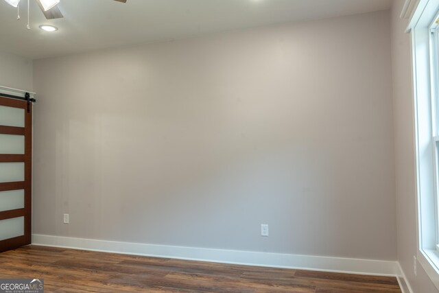spare room with baseboards, a ceiling fan, dark wood-type flooring, and a barn door