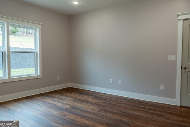 spare room with baseboards and dark wood-type flooring